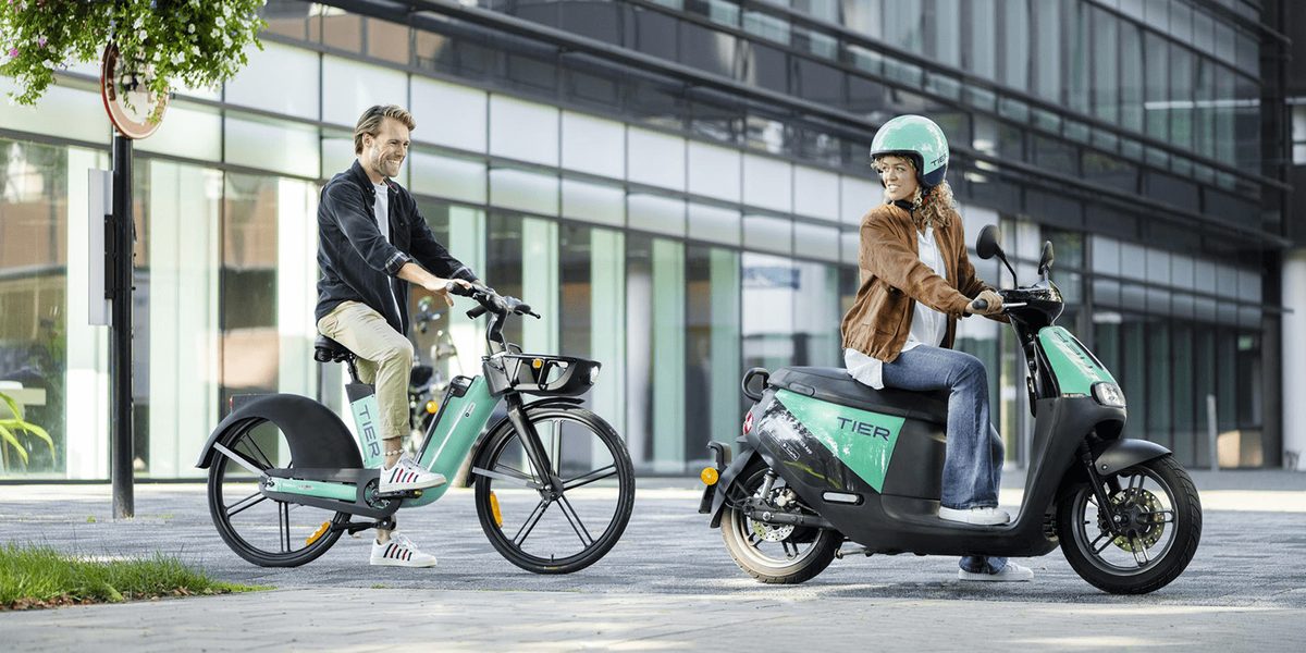 Two people riding TIER e-bikes and scooters through a city street